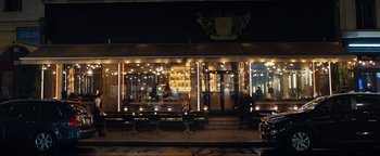 Movie still from “Uncharted” (2022), directed by Ruben Fleischer – People sitting at a table outside of a restaurant at night; Extreme Wide shot, High angle