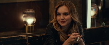 Movie still from “Uncharted” (2022), directed by Ruben Fleischer – A beautiful young lady sitting in front of a fireplace; Close Up shot, Over the shoulder angle