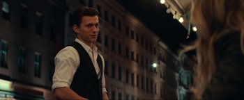 Movie still from “Uncharted” (2022), directed by Ruben Fleischer – A man in a vest standing in front of a tall building; Medium shot, Over the shoulder angle