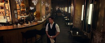 Movie still from “Uncharted” (2022), directed by Ruben Fleischer – A man standing in front of a bar holding a napkin; Wide shot, High angle