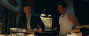 Movie still from “Uncharted” (2022), directed by Ruben Fleischer – Two men standing next to each other in front of a television; Medium shot, Over the shoulder angle