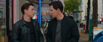 Movie still from “Uncharted” (2022), directed by Ruben Fleischer – Two men are talking on the sidewalk of a city street; Medium shot, Over the shoulder angle