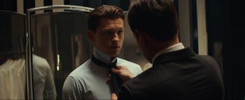 Movie still from “Uncharted” (2022), directed by Ruben Fleischer – A man adjusting a neck tie of another man in front of a mirror; Close Up shot, Over the shoulder angle