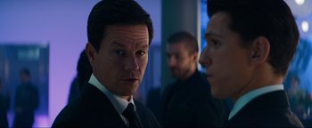 Movie still from “Uncharted” (2022), directed by Ruben Fleischer – A man in a suit and tie standing next to another man in a suit and tie; Close Up shot, Over the shoulder angle