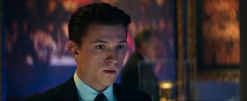 Movie still from “Uncharted” (2022), directed by Ruben Fleischer – A man in a suit and tie looking at the camera; Close Up shot, Over the shoulder angle