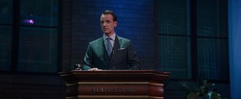 Movie still from “Uncharted” (2022), directed by Ruben Fleischer – A man standing at a podium in front of a brick wall; Medium shot, Low angle