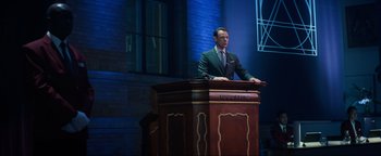 Movie still from “Uncharted” (2022), directed by Ruben Fleischer – A man standing at a podium in front of an audience; Wide shot, Over the shoulder angle