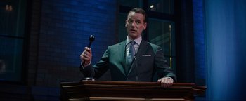 Movie still from “Uncharted” (2022), directed by Ruben Fleischer – A man in a suit and tie holding a gavel; Medium shot, Low angle