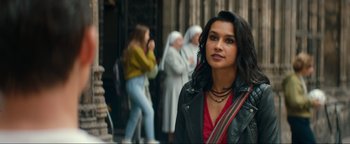 Movie still from “Uncharted” (2022), directed by Ruben Fleischer – A woman in a red top and black leather jacket standing in front of a group of people; Close Up shot, Over the shoulder angle