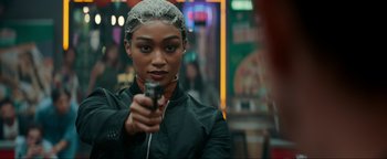 Movie still from “Uncharted” (2022), directed by Ruben Fleischer – A woman holding a gun while standing next to a building; Close Up shot, Over the shoulder angle