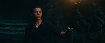 Movie still from “Uncharted” (2022), directed by Ruben Fleischer – A young man holding something in his hand; Medium shot, Low angle