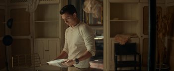 Movie still from “Uncharted” (2022), directed by Ruben Fleischer – A man holding papers in his hands while standing in a living room; Medium shot, Over the shoulder angle