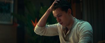 Movie still from “Uncharted” (2022), directed by Ruben Fleischer – A young man is scratching his head with one hand; Close Up shot, Over the shoulder angle