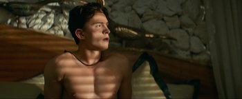 Movie still from “Uncharted” (2022), directed by Ruben Fleischer – A man with a necklace is sitting in a room; Close Up shot, Low angle