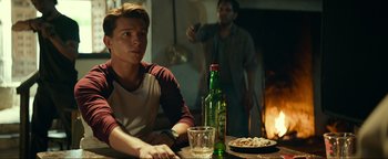 Movie still from “Uncharted” (2022), directed by Ruben Fleischer – A man sitting at a table in front of an open fire; Medium shot, Over the shoulder angle