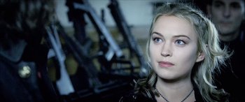 Movie still from “Underworld” (2003), directed by Len Wiseman – A beautiful young lady looking at the camera while standing in front of a bunch of guns; Close Up shot, Over the shoulder angle