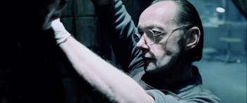 Movie still from “Underworld” (2003), directed by Len Wiseman – An older man with glasses is holding his arm up; Close Up shot, Low angle