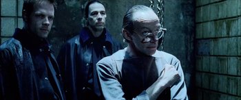 Movie still from “Underworld” (2003), directed by Len Wiseman – A man with glasses is standing next to another man in chains; Close Up shot, Over the shoulder angle