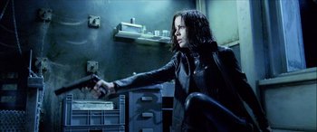 Movie still from “Underworld” (2003), directed by Len Wiseman – A woman holding a gun while sitting in a room; Medium shot, Low angle