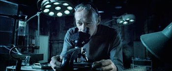 Movie still from “Underworld” (2003), directed by Len Wiseman – An older man looking through a microscope in a dark room; Close Up shot, High angle