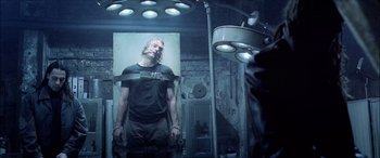 Movie still from “Underworld” (2003), directed by Len Wiseman – A man in a black shirt is in a room with lights on; Medium shot, Low angle