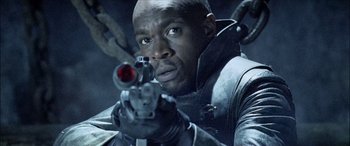 Movie still from “Underworld” (2003), directed by Len Wiseman – A man holding a gun while looking at the camera; Close Up shot, Low angle