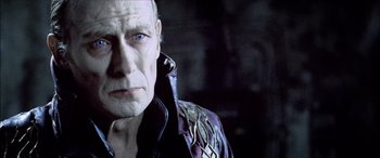 Movie still from “Underworld” (2003), directed by Len Wiseman – An older man wearing a leather jacket and looking at the camera; Close Up shot, Over the shoulder angle