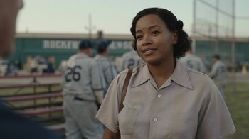 Movie still from “A League of Their Own” (2022), created by Abbi Jacobson – A woman in a baseball uniform standing in front of a group of men; Close Up shot, Over the shoulder angle