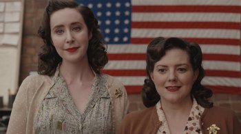 Movie still from “A League of Their Own” (2022), created by Abbi Jacobson – A couple of women standing next to each other in front of an american flag; Close Up shot, Over the shoulder angle