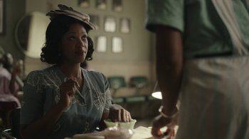Movie still from “A League of Their Own” (2022), created by Abbi Jacobson – A woman sitting at a table with a plate of food in front of her; Medium shot, Over the shoulder angle