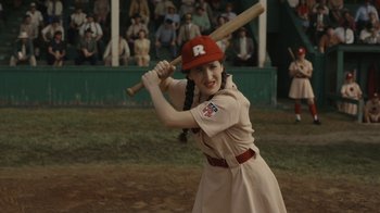 Movie still from “A League of Their Own” (2022), created by Abbi Jacobson – A girl in a baseball uniform holding a baseball bat; Medium shot, High angle