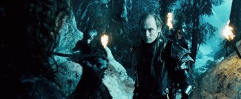 Movie still from “Underworld: Evolution” (2006), directed by Len Wiseman – A man in a black jacket is standing next to a fire; Medium shot, Low angle
