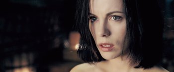 Movie still from “Underworld: Evolution” (2006), directed by Len Wiseman – A woman's face in a dimly - lit room; Close Up shot, Over the shoulder angle