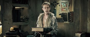 Movie still from “Underworld: Evolution” (2006), directed by Len Wiseman – A man holding an open book in a room; Medium shot, Low angle
