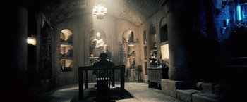 Movie still from “Underworld: Evolution” (2006), directed by Len Wiseman – A man sitting at a table in a room; Wide shot, Low angle