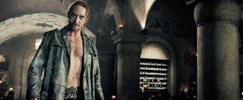 Movie still from “Underworld: Evolution” (2006), directed by Len Wiseman – A man standing in front of a pillar with candles; Medium shot, Over the shoulder angle