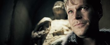 Movie still from “Underworld: Evolution” (2006), directed by Len Wiseman – A man's face in front of a statue; Close Up shot, Over the shoulder angle