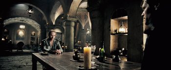 Movie still from “Underworld: Evolution” (2006), directed by Len Wiseman – A man sitting at a table with a candle; Wide shot, High angle