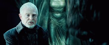 Movie still from “Underworld: Evolution” (2006), directed by Len Wiseman – An old man with a white beard standing in front of a statue; Close Up shot, Over the shoulder angle