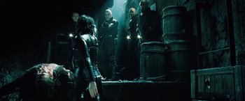 Movie still from “Underworld: Evolution” (2006), directed by Len Wiseman – A group of people standing in a dark room; Medium shot, Over the shoulder angle