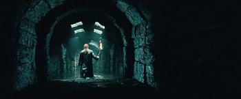 Movie still from “Underworld: Evolution” (2006), directed by Len Wiseman – A man holding a torch in a dark cave; Wide shot, High angle