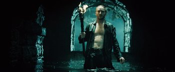 Movie still from “Underworld: Evolution” (2006), directed by Len Wiseman – A man holding a torch while standing next to water; Medium shot, Low angle