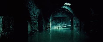 Movie still from “Underworld: Evolution” (2006), directed by Len Wiseman – A dark cave with water in the foreground and light coming from the ceiling; Extreme Wide shot, High angle