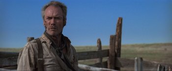 Movie still from “Unforgiven” (1992), directed by Clint Eastwood – A man standing next to a wooden fence in a field; Close Up shot, Low angle
