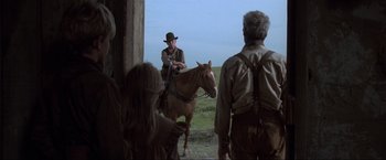 Movie still from “Unforgiven” (1992), directed by Clint Eastwood – A man sitting on a horse in front of a group of people; Wide shot, Over the shoulder angle