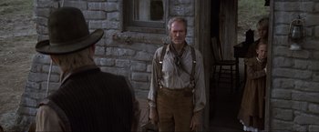 Movie still from “Unforgiven” (1992), directed by Clint Eastwood – A man standing in front of a brick building; Medium shot, Over the shoulder angle
