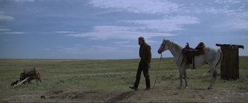 Movie still from “Unforgiven” (1992), directed by Clint Eastwood – A man walking with a horse in a field; Wide shot, Low angle