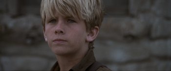 Movie still from “Unforgiven” (1992), directed by Clint Eastwood – A young boy with blonde hair and blue eyes looking at the camera; Close Up shot, Low angle