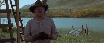 Movie still from “Unforgiven” (1992), directed by Clint Eastwood – An older man wearing a hat and gloves standing in front of a lake; Medium shot, Over the shoulder angle