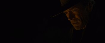 Movie still from “Unforgiven” (1992), directed by Clint Eastwood – A man in a hat is looking into the dark; Close Up shot, Low angle